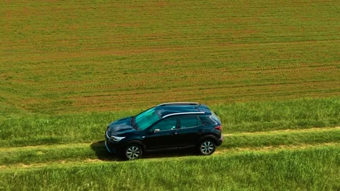 Driving hatchback car along grassy track near cultivated farmland. Across uneven Stock Footage 311320119