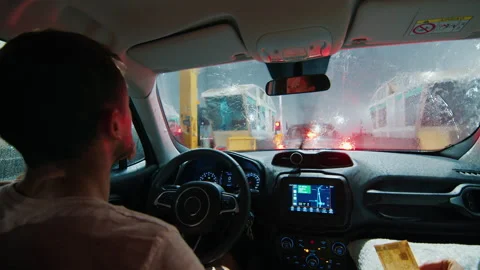 Driving at heavy rain. Man driver sits in the car and waits in a queue to pay Stock Footage 237775836