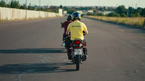 Driving instructor on a moped in a yellow T-shirt follow their student in a red Stock Footage 249606749