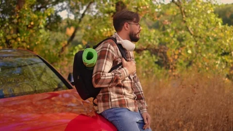 Driving out for a picnic, a man steps out of the car with a backpack, gazing int Stock Footage 278277298