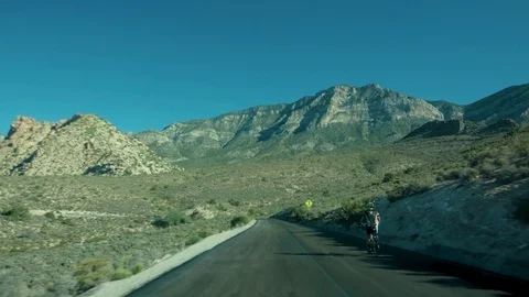 Driving past a cyclist on a long empty road in Red Rocks Stock Footage 79852033