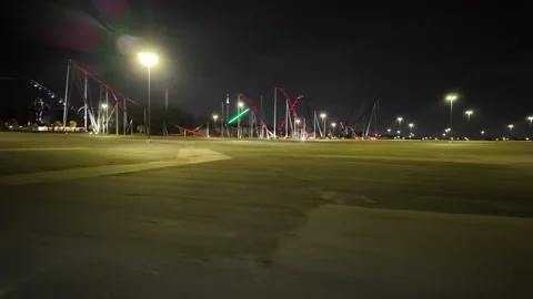 Driving Past a Rollercoaster Theme Park at Night in an Empty Lot Stock Footage 332175883