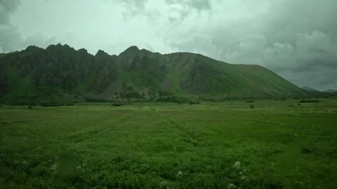 Driving past vibrant green fields and jagged mountain range in Andoya Norway Vidéo 343131138