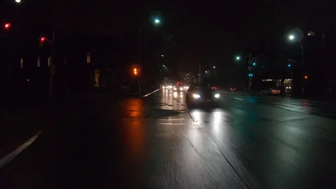 Driving plate POV reverse angle dark city streets at night with car traffic Stock Footage 100124643