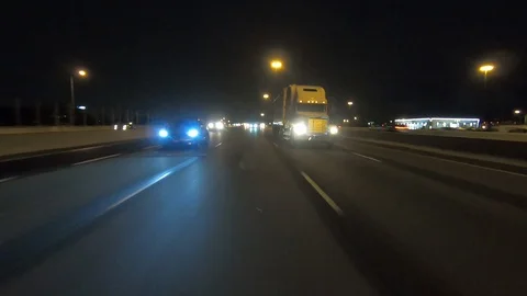 Driving plate POV reverse of traffic on highway on dark rainy night Stock Footage 112928904