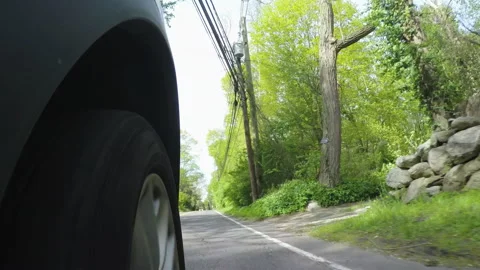 Driving POV: Low Angle Tire Closeup POV as car drives on suburban forest roads Stock-Footage 131134738