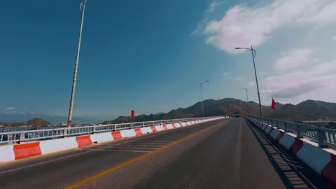 Driving on Scenic Bridge Road with Red Flags and Mountain View Stock Footage 337028123