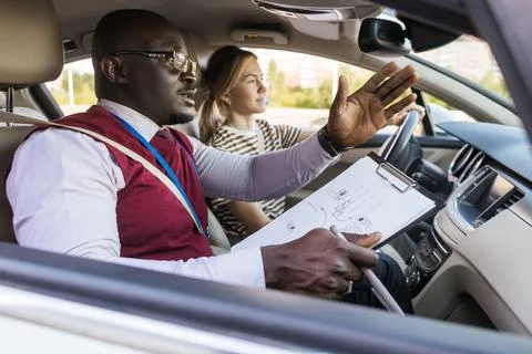 Driving school concept. A car instructor teaches a young woman how to drive Stock Photos