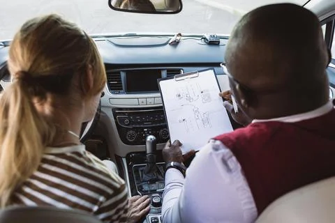 Driving school concept. A car instructor teaches a young woman how to drive Stock Photos