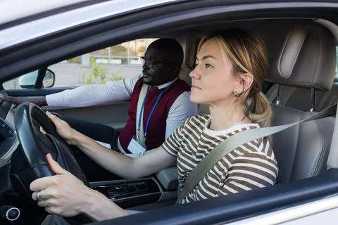 Driving school concept. A car instructor teaches a young woman how to drive Stock Photos