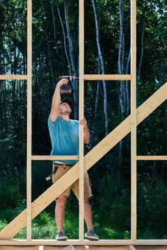 Driving screw into timber frame, young construction worker fastens vertical.. Stock Photos