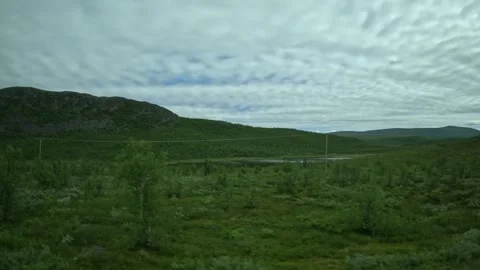 Driving side window view of green tundra hills and cloudy sky in Lapland Finland Vidéo 340960135