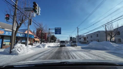 Driving snowy street toward intersection with road signs in Asahikawa Vídeos de archivo 333314224