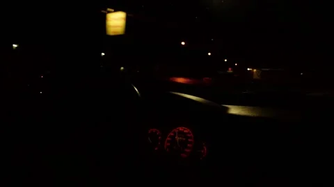 Driving through a small town with a gas station at night, focus on wheel Stock Footage