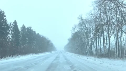 Driving through snow on a winter road surrounded by trees in a foggy setting Stock Footage 326694935