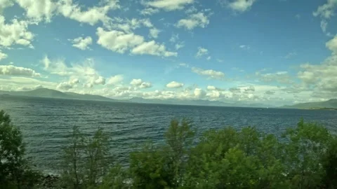 Driving tracking shot along open sea bay and coastline under blue sky in Norway Stock-Footage 343833892