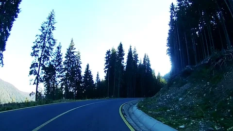 Driving uphill on a winding mountain road with the sun shining through the trees Stock Footage 71489448