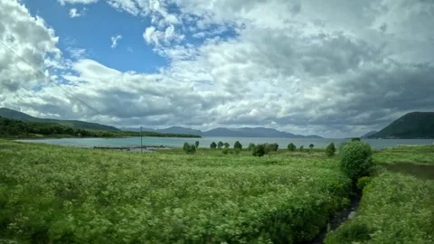 Driving view past green field towards coastal fjord and mountains in Norway Vídeo Stock 343380225
