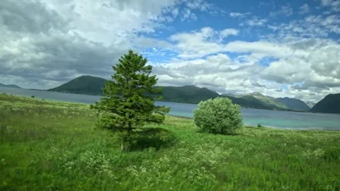 Driving view past green meadow towards turquoise fjord and mountains in Norway Vidéo 343380214
