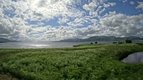 Driving view past river estuary towards glittering fjord in Norway Vidéo 343380320