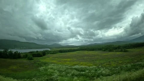 Driving wide view past green fields and lake under overcast sky in Senja Norway 動画素材 342340371