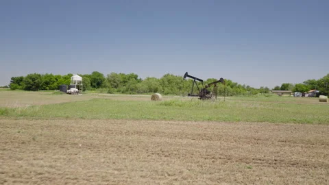 Drone 4K of a field of hay bails surrounding an oil pump jack in the spring and Stock Footage 335138635