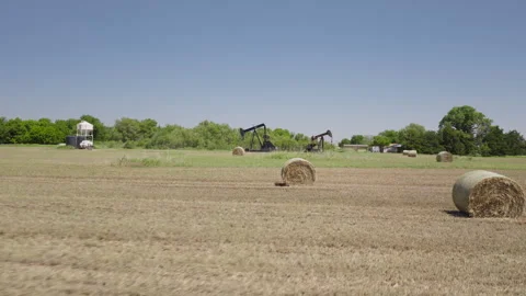 Drone 4K of a field of hay bails surrounding an oil pump jack in the spring and Stock Footage 335138652