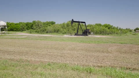 Drone 4K of a field of hay bails surrounding an oil pump jack in the spring and Stock Footage 335139353