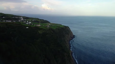 Drone 4K flying left-to-right over cliff with green hills, houses, and crashing Stock Footage 315264235