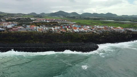 Drone 4K over black cliff, rocky beach, town, and green fields Stock Footage 315260204
