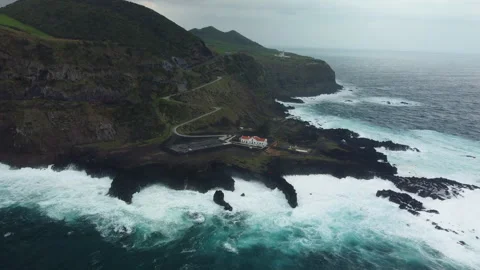 Drone 4K top-down over rocky peninsula with house, waves, and winding road Stock Footage 315254236