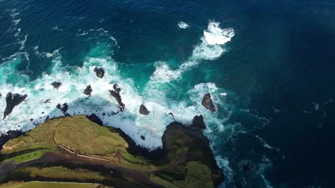 Drone 4K top-down over green cliff, town, and crashing waves Stock Footage 315256524
