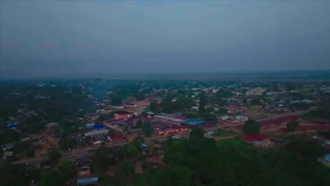 Drone advancing toward warehouses surrounded by trees, Ouesso, Congo Видео 331999721
