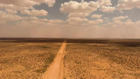 Drone aerial of car traveling through vast australian outback towards dust storm Stock Footage