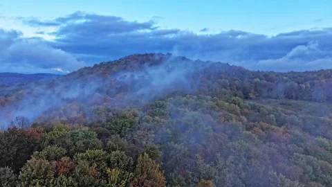Drone aerial hyperlapse of fog dissolving over a hill with fall foliage Stock Footage 317834565