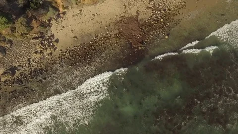 Drone aerial looking straight down onto beach with crashing waves twisting Stock Footage 83929251