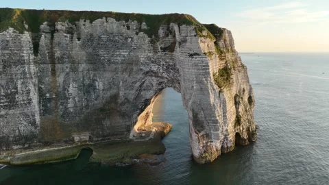 Drone aerial pull back over Etretat arch cliff golden hour calm sea France Stock Footage 346477246