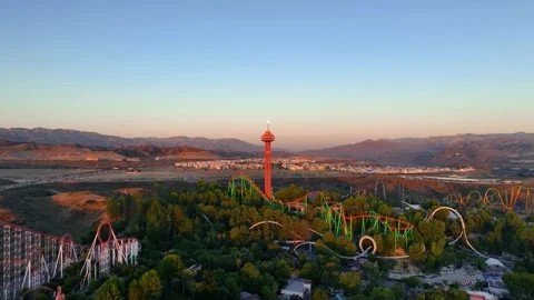 Drone aerial pull out over theme park roller coasters, observation tower, trees  Stock Footage 250473198