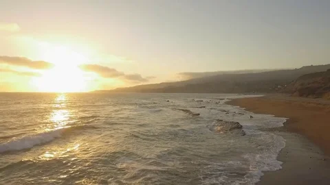 Drone aerial shot flying low over gentle waves onto beach with sunset Stock Footage 83929184