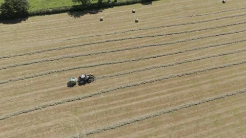 Drone aerial shot of a tractor pulling a baler through a field, collecting Stock Footage 281766717