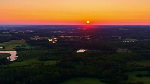 Drone aerial at sunset over patchwork fields, forests and small lakes, with a Stock Footage 333314247