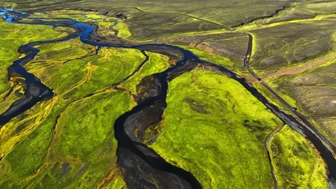 Drone aerial of a tiny car driving a remote road beside a winding river through 스톡 동영상 331609134