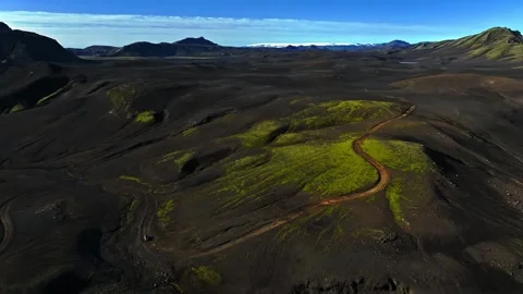 Drone aerial of a tiny car on a winding dirt road through black volcanic hills 動画素材 331117248