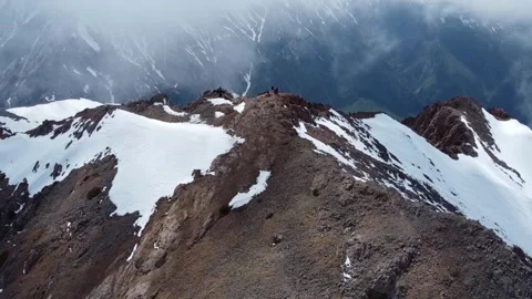 Drone Aerial: Tiny Climbers on Snow-Covered Mountain Peak Above Clouds Stock Footage 330961343