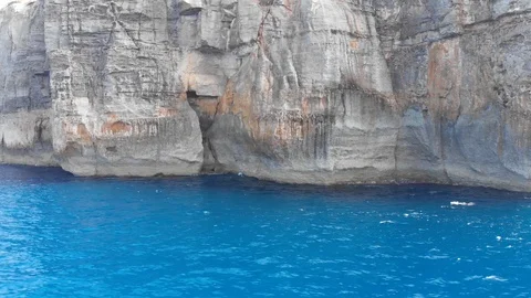 Drone aerial tracking shot of waves hitting rock cliffs inside a blue sea Stock Footage 111267586