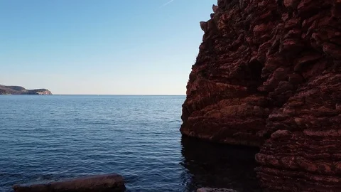 Drone Aerial view between a large red rocky ledge, to a small island Stock Footage 124899975