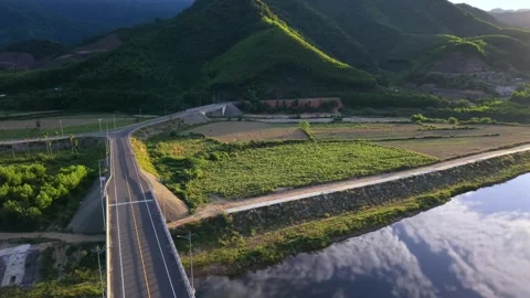 Drone aerial view of a mountain road bridge crossing a calm river at sunset Stock Footage 336610377
