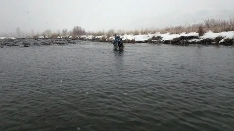 A drone aerial view of two people fly fishing during winter snow fall. Stock Footage 100002906