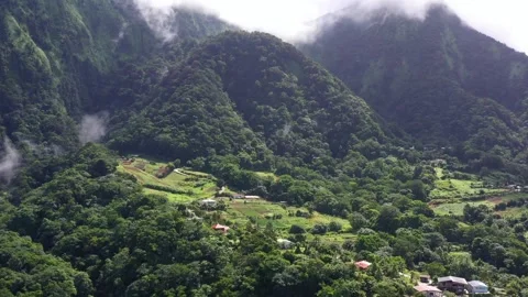 Drone Approaching Cloudy Pitons du Carbet with Lush Forest and Farmland Below Stock Footage 317104417