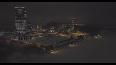 Drone approaching illuminated modern complex over winter river Stock Footage 320240826